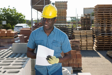 African american man manager working in an open air warehouse keeps records of construction...