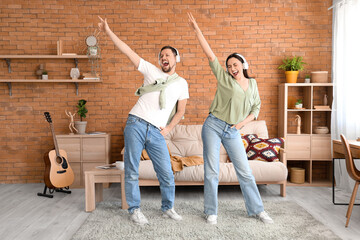 Young couple in headphones dancing on green carpet at home