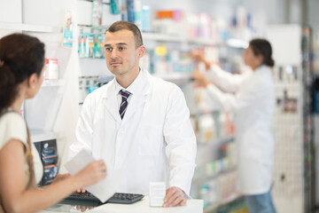 Polite male pharmacist consulting woman client about medicament in box according to her recipe in chemist's shop - Powered by Adobe