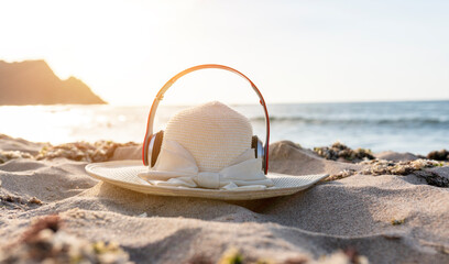 A straw hat with headphones lies on the sand at the beach. summer holiday travel and sea concept