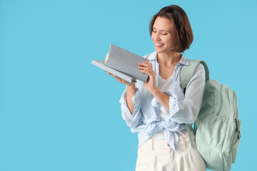 Happy female student with backpack and books on blue background