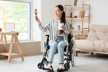 Young Asian woman in wheelchair with paint brush and can during repair at home