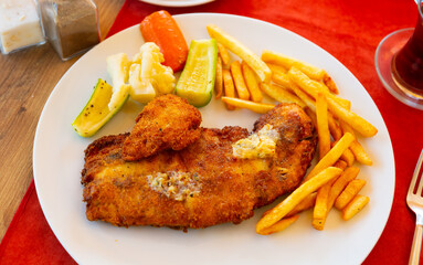 Piece of deep-fried fish filet in crispy coating of egg and breadcrumbs served with side dish of...