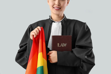 Female judge with LGBT flag and law book on light background, closeup