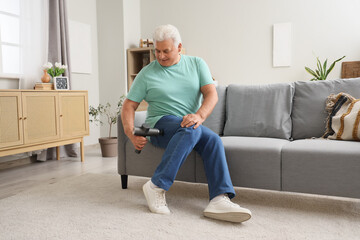 Mature man massaging his thigh with percussive massager on sofa at home