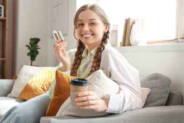 Young woman smoking disposable electronic cigarette and holding cup of coffee at home