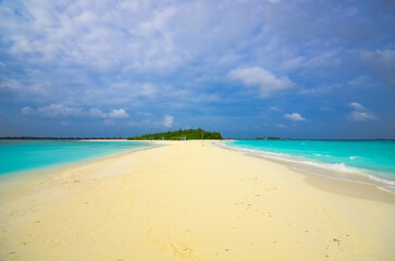 Wide-angle view of a tranquil sandy beach with turquoise waters under a blue sky