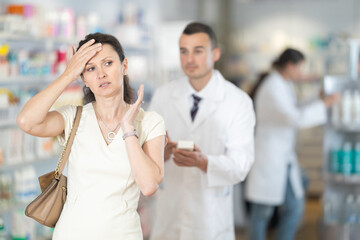 Young male pharmacist advising medicine for headache to adult woman at pharmacy