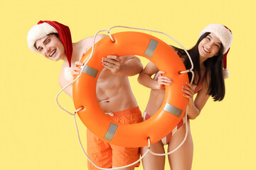 Young couple in Santa hats with ring buoy on yellow background. Christmas in July