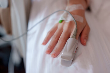 Close-up of adult hand with IV line, resting on hospital bed. Transparent tape secures green...