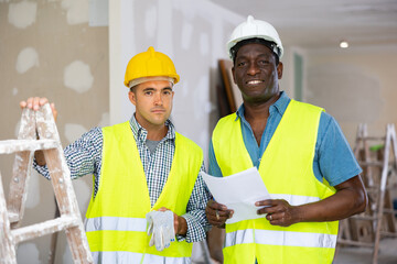 Portrait of smiling men builders inside apartment during repair works. African-american man...