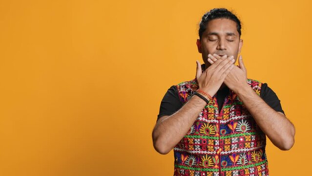 Man wearing traditional indian clothing covering eyes, ears and mouth, imitating three wise monkeys, doing dont see, dont hear and dont speak hand gesturing concept, studio background, camera A