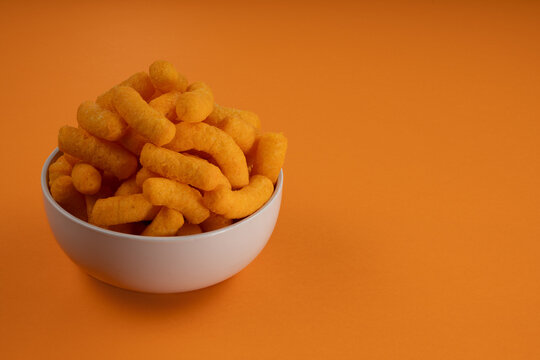 Cheese Puff Crisps/Chips in a Bowl on an Orange Background