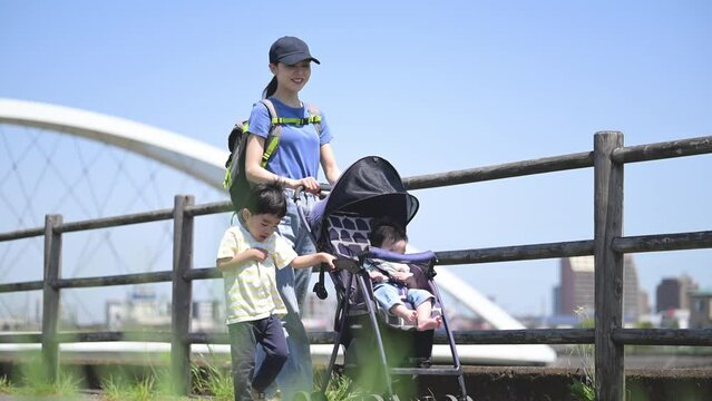 Full body of mom and siblings (family of 3) strolling in a stroller in a park along a river in sunny weather Video of images of spring and summer outings and mom's commute to work.