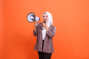 Cheerful young indonesia woman in hijab facing right sideways shouting using mic holding megaphone...