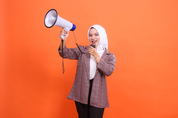 Angry mature Asian woman in hijab facing right to camera shouting using mic holding megaphone...