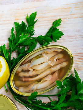 Picture of tasty sea natural navajas in open tin can served with greens and lemon at table