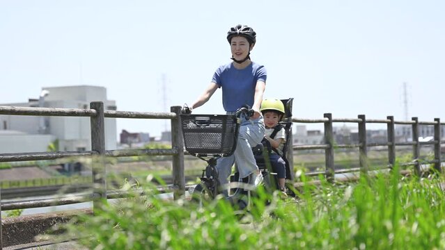 春夏の青空の綺麗な道を自転車に乗るママと子供　ママチャリでお出かけや出勤　全身のスロー動画