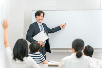 塾・学校の教室で小学生・中学生の子供に勉強を教える男性講師・教師
