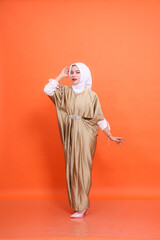 Full body of young elegant Asian Muslim woman wearing kaftan hijab standing floating pose isolated orange background. The concept of Islamic religion, fashion and commercial