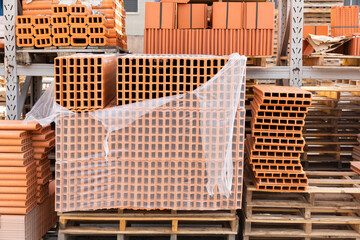 Red brick packed in stacks are stored on ground outdoors at a hardware store warehouse