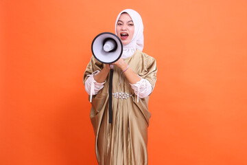 Beauty mature Asian woman shouting with both hands holding megaphone loudspeaker wearing kaftan...