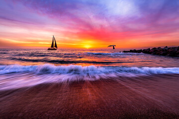 Peaceful scene of a sailboat on the horizon at sunset, with vibrant sky and gentle waves