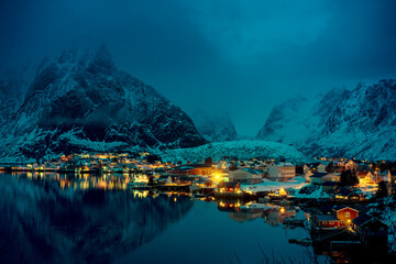Tranquil twilight over a snowy arctic village with illuminated houses reflecting in the calm water