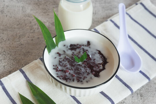 Black sticky rice porridge, a typical Indonesian dessert. Black sticky rice porridge with coconut milk, sugar and pandan leaves. Served in a white bowl.