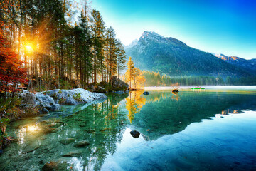 Tranquil sunrise over a reflective alpine lake with lush forest and majestic mountains