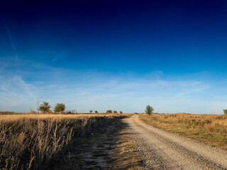 Panorama of a gravel road, a dirtpath in Dolovo, in the serbian countryside, in autumn, surrounded by dry grass fields. It's a symbol of Serbian and central european agriculture.