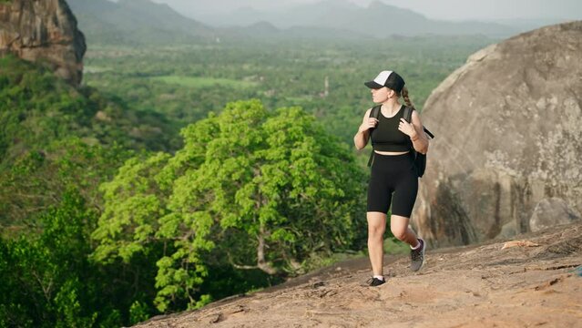 Active woman hikes up rocky trail with Sigiriya Rock in distance. Female adventurer in fitness gear explores Sri Lanka, breathes fresh air atop Pidurangala Rock, rich scenery, feels nature peace.
