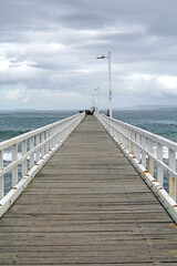 Long wooden pier jetty extending into the sea under an overcast cloudy sky at Point Lonsdale in Victoria, Australia