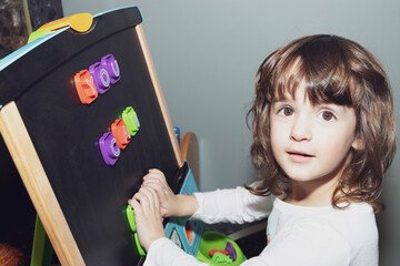 Toddler girl learning letters on the magnetic easel at home.