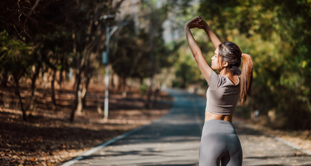 Rear view of a fitness-conscious woman with arms raised, engaging in a stretching routine on a secluded outdoor path.