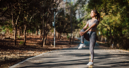 Athletic woman performing a standing leg stretch on a tranquil outdoor path, surrounded by trees and nature.