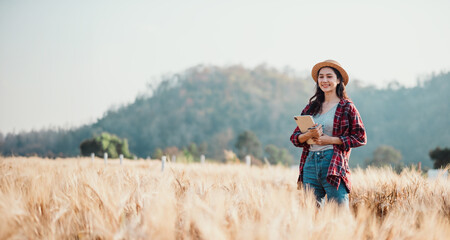 Woman stands holding a notebook in a vast wheat field, with the backdrop of a clear blue sky and distant hills.