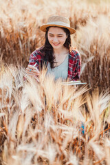 Joyful young woman with a straw hat writes in her notebook, immersed in the golden hues of a wheat field.