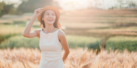 Carefree young woman in a summer dress and straw hat enjoying the golden glow of the sunset in a beautiful wheat field.