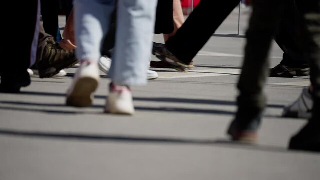 Close-up of individuals' feet crossing a pedestrian zebra crossing, various footwear styles