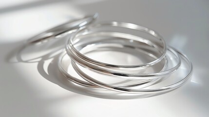 Fototapeta premium A set of minimalist silver bangles on a stark white background, highlighted by soft shadows