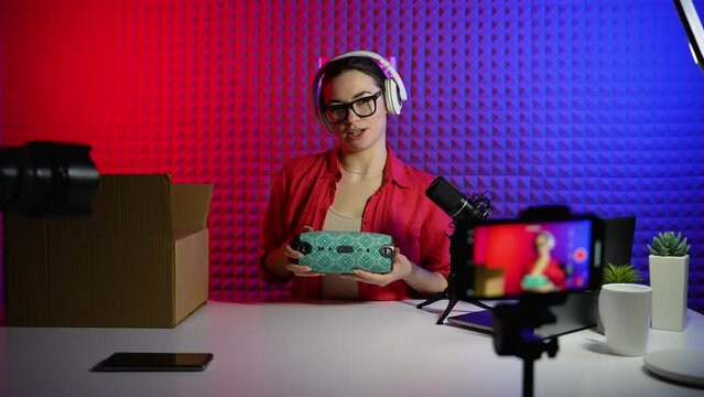 Female tech blogger unpacking box and recording video review of new Bluetooth speaker