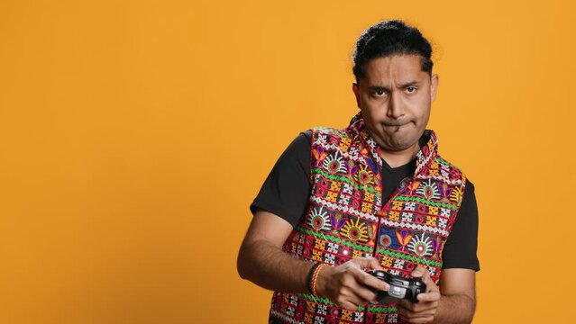 Gamer annoyed after losing online multiplayer videogame, being defeated by rival players. Indian man shocked and gutted after seeing game over message, holding controller, studio background, camera A