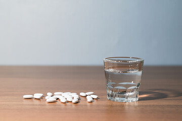 white pills and caplsules, glass of water on wooden table