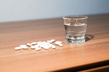 white pills and caplsules, glass of water on wooden table