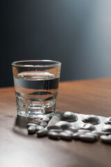 white pills and caplsules, glass of water on wooden table