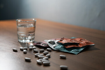 white pills and caplsules, glass of water on wooden table