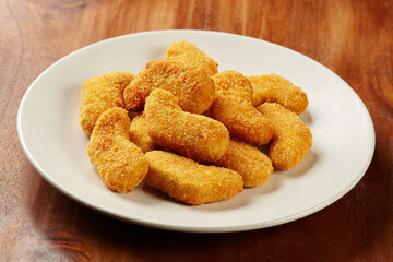 A portion of chicken nuggets served in a white plate on a wooden table background