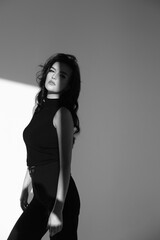 Fototapeta premium Brunette female in black clothes on the background of a white and gray wall. Minimalistic style. Sensual black and white portraits of a woman