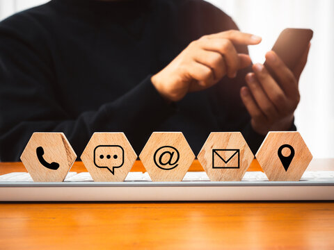 Contact us concept. Company website, FAQ, hotline phone number call, address, e-mail marketing and chat for customer support. Icons on hexagon wood blocks with businessman using mobile smart phone.